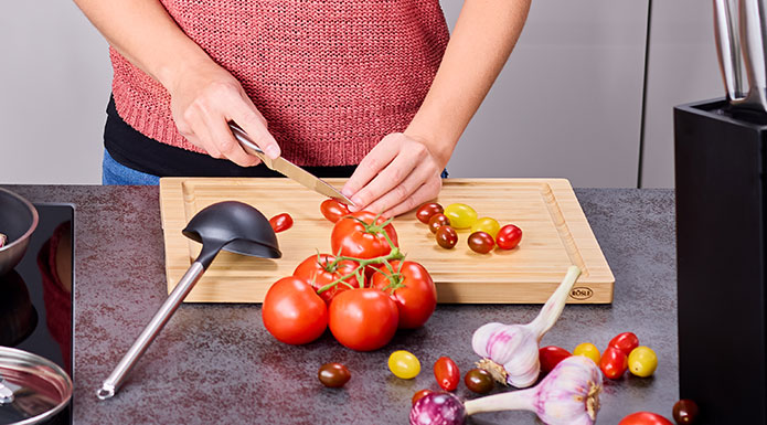 Basic Line Frau schneidet mit Messer Tomaten auf Schneidbrett