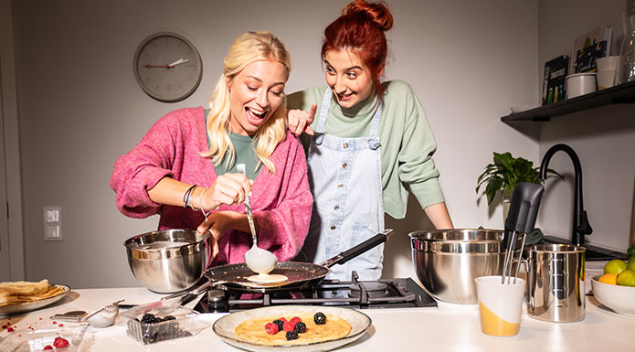 Zwei Freundinnen machen zusammen Crepes. Frau gießt Teig in die Pfanne