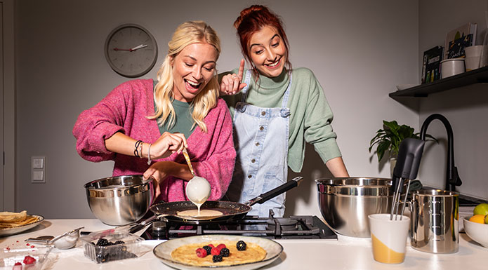 Zwei Freundinnen machen zusammen Crepes. Frau gießt Teig in die Pfanne