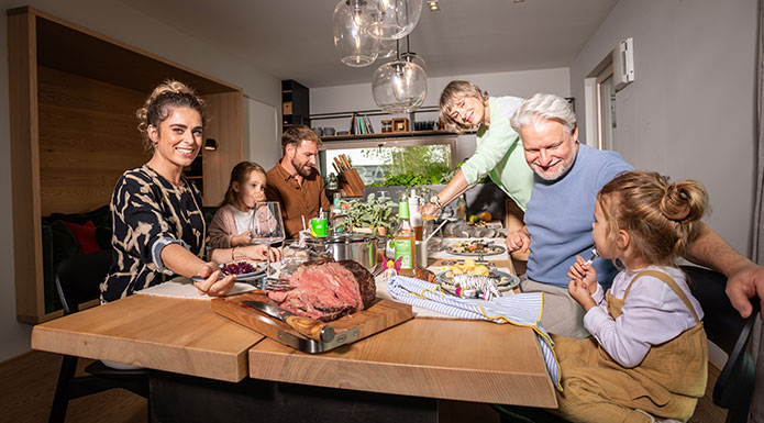 Sechs Familienmitglieder sitzen zusammen am Tisch und verteilen das Essen