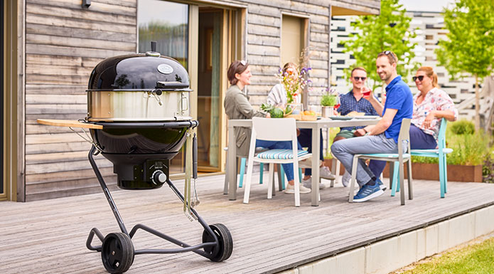 Holzkohle-Kugelgrill AIR F60 PRO Holzkohle Kugelgrill AIR F60 PRO mit Gourmetring im Vordergrund und im Hintergrund sitzen Freunde zusammen am Tisch