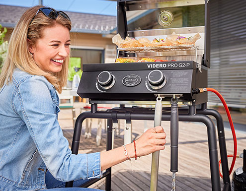 Frau hängt Grillzange an Hakenleiste am mobilen Gasgrill