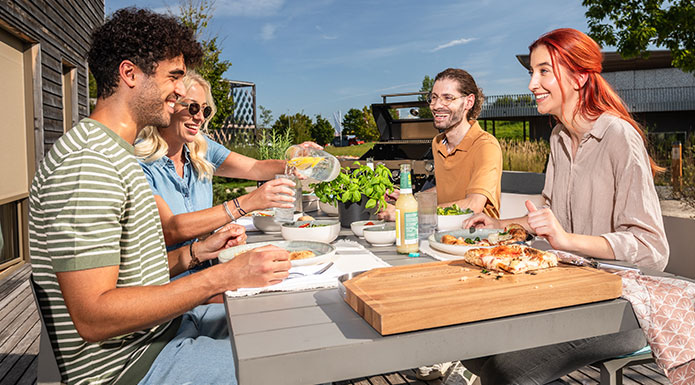 Vier Freunde sitzen zusammen am Terrassentisch und essen zusammen Pizza